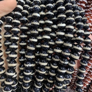 May include: A strand of black and white agate beads. The beads are round and have a faceted finish. The beads are strung on a clear elastic cord.