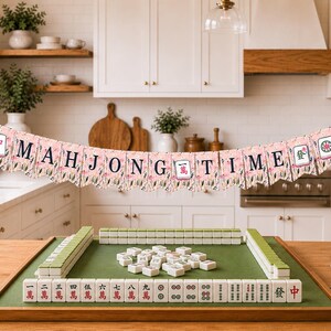 May include: A Mahjong set with a green playing surface and white tiles. A banner that says "MAHJONG TIME" hangs above the set. The banner has a floral design and is pink and white.