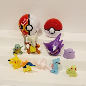 May include: A collection of Pokemon figures, including Pikachu, Squirtle, and a purple Gengar. There are also two Poke Balls, one red and one red and white.