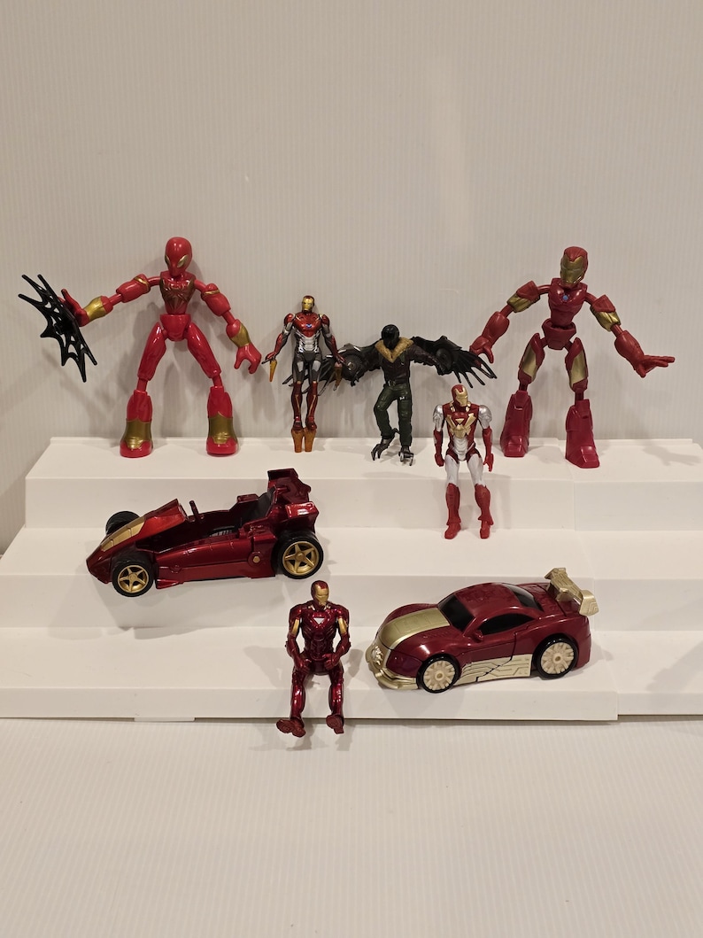 May include: A collection of superhero action figures and toy cars. The figures are in various poses and feature red, gold, and black color schemes. The toy cars are primarily red with gold accents.