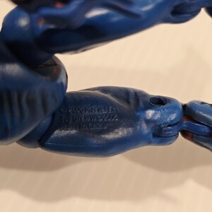Pode incluir: Close-up de uma figura de a&ccedil;&atilde;o azul e vermelha. O bra&ccedil;o da figura &eacute; azul com detalhes vermelhos. O texto na figura diz "&copy;2006 Marvel Ent. Toy Biz/WW/&copy;2002. Made in China."