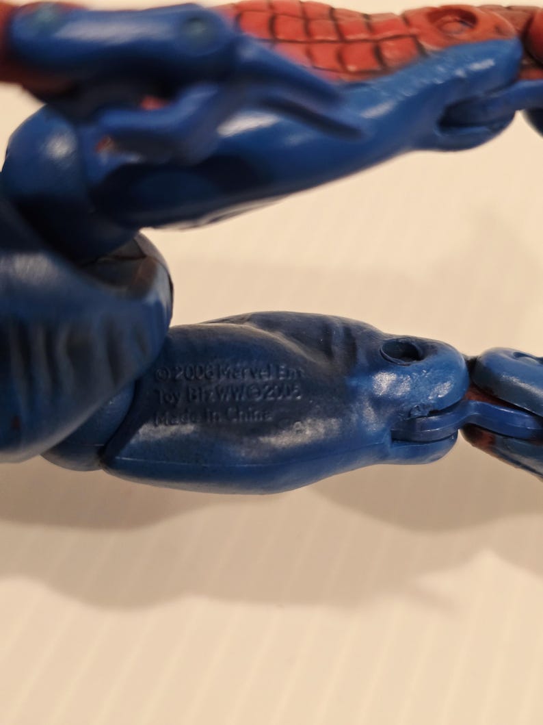 Pode incluir: Close-up de uma figura de a&ccedil;&atilde;o azul e vermelha. O bra&ccedil;o da figura &eacute; azul com detalhes vermelhos. O texto na figura diz "&copy;2006 Marvel Ent. Toy Biz/WW/&copy;2002. Made in China."