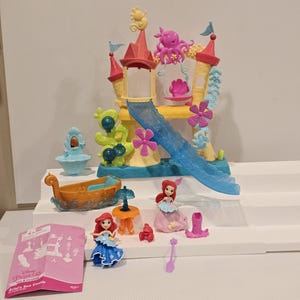 K&ouml;nnte beinhalten: Ariel's Sea Castle Spielset mit einem mehrst&ouml;ckigen Schloss mit Rutsche, Boot und mehreren Ariel-Figuren. Das Schloss ist gelb, rosa und blau. Zus&auml;tzliches Zubeh&ouml;r ist enthalten.