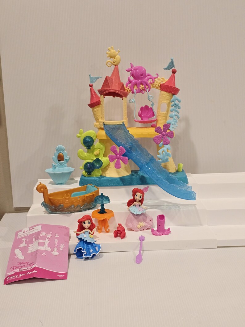 K&ouml;nnte beinhalten: Ariel's Sea Castle Spielset mit einem mehrst&ouml;ckigen Schloss mit Rutsche, Boot und mehreren Ariel-Figuren. Das Schloss ist gelb, rosa und blau. Zus&auml;tzliches Zubeh&ouml;r ist enthalten.