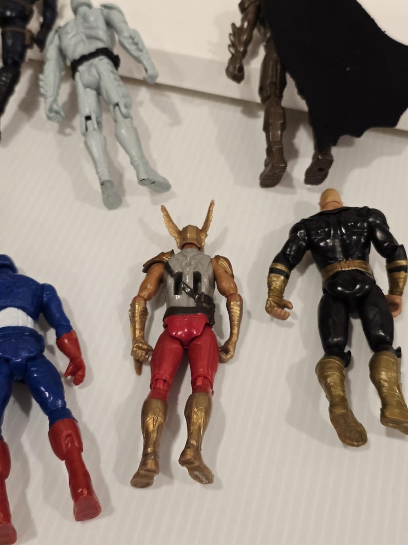 May include: A collection of superhero action figures. The figures include Captain America in red, white, and blue, a figure in red and gold, and a figure in black and gold. Other figures are also visible.