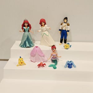 K&ouml;nnte beinhalten: Eine Sammlung von Miniaturfiguren mit Charakteren aus einem beliebten Zeichentrickfilm. Das Set enth&auml;lt eine Meerjungfrau, einen Prinzen und andere Charaktere. Die Figuren sind farbenfroh und aus Kunststoff.