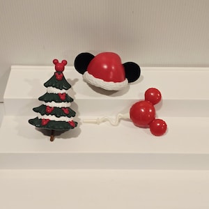 May include: A set of three small plastic ornaments including a dark green Christmas tree decorated with red mouse-shaped icons, a red Santa hat with black mouse ears, and a red mouse-shaped balloon on a thin white stick with a wavy stem.