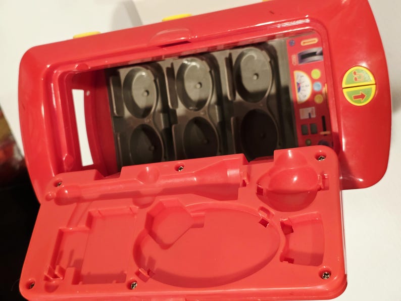 K&ouml;nnte beinhalten: Ein rotes Kunststoffspielzeug mit offenem Deckel, das F&auml;cher und geformte Formen freigibt. Das Spielzeug hat gelbe Akzente und einen detaillierten Innenraum mit verschiedenen geformten Merkmalen. Der offene Deckel ist ebenfalls rot.