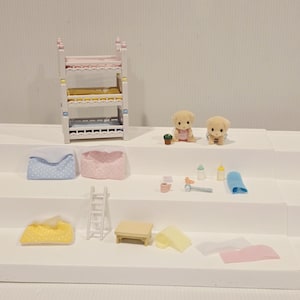 Puede incluir: Un juego de casa de mu&ntilde;ecas en miniatura con una litera, dos cachorros de juguete y varios accesorios. El juego incluye almohadas, una escalera, una mesa y biberones. La litera tiene ropa de cama rosa, amarilla y azul.