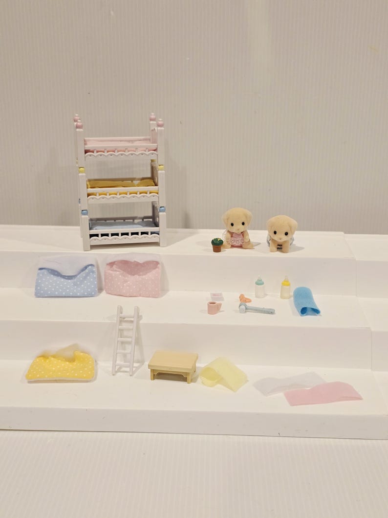 Puede incluir: Un juego de casa de mu&ntilde;ecas en miniatura con una litera, dos cachorros de juguete y varios accesorios. El juego incluye almohadas, una escalera, una mesa y biberones. La litera tiene ropa de cama rosa, amarilla y azul.