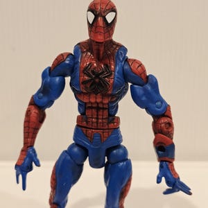 Pode incluir: Figura de a&ccedil;&atilde;o do Homem-Aranha com um traje vermelho e azul. A figura tem uma m&aacute;scara vermelha com lentes brancas, um emblema de aranha preta no peito e articula&ccedil;&otilde;es. A figura tem aproximadamente 15 cm de altura.