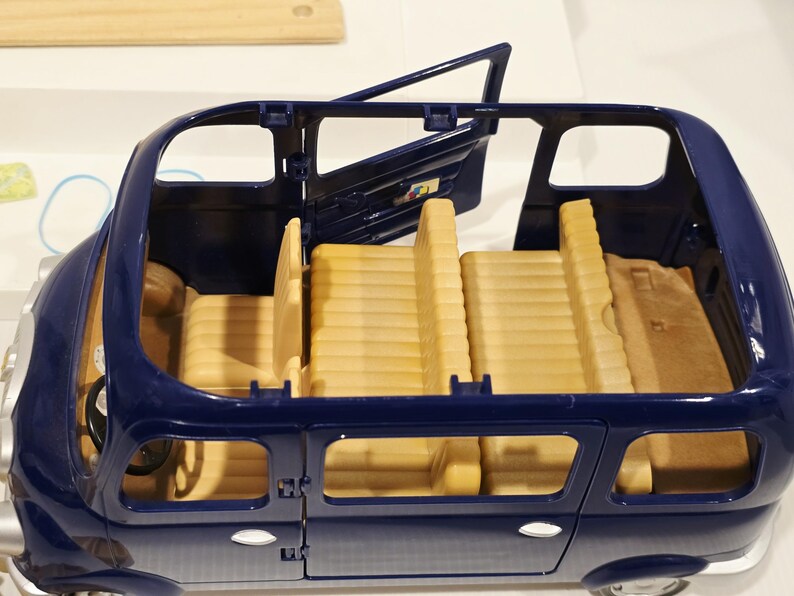 May include: A blue toy car with an open door, revealing tan seats and interior details. The car has a steering wheel and windows. The toy car is designed for children's play and imaginative scenarios.