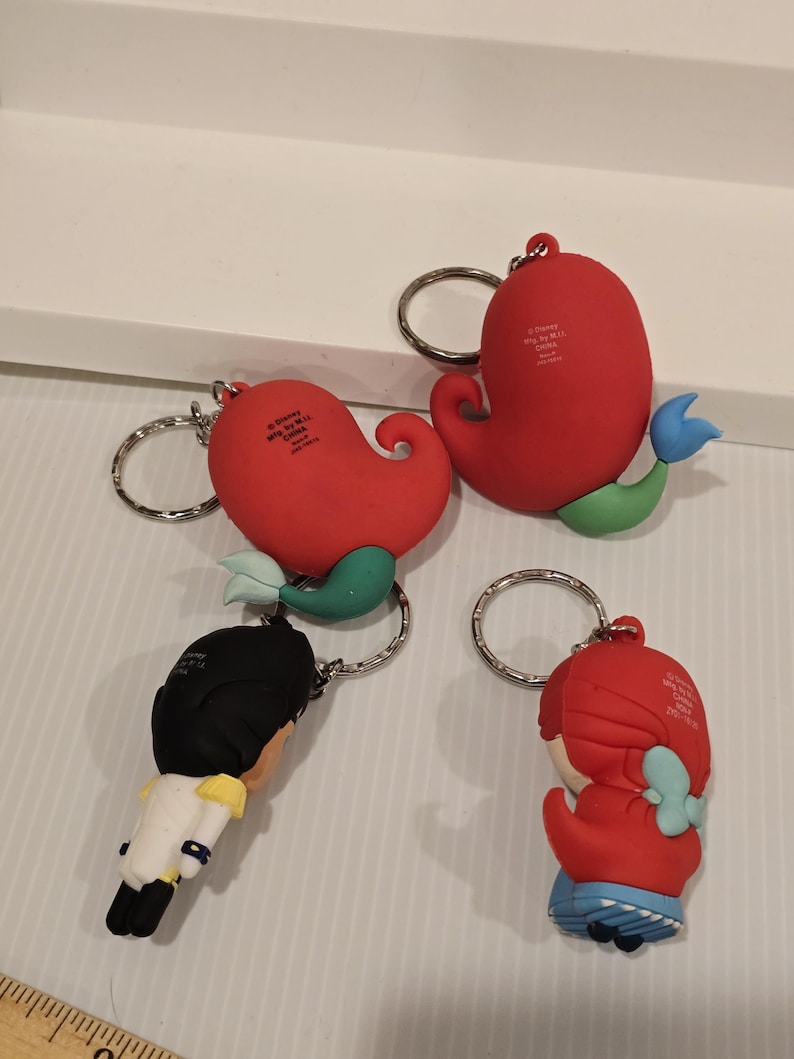 May include: Four keychains featuring characters from a Disney movie. The keychains have a red, blue, green, black, and white color scheme. The keychains are attached to silver keyrings. The keychains are made of a rubbery material.