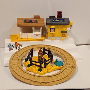 May include: A GeoTrax train set with a yellow track, a barn, a train station, and a yellow train station. The set includes miniature figures of a farmer and a horse. The train station has the GeoTrax logo.