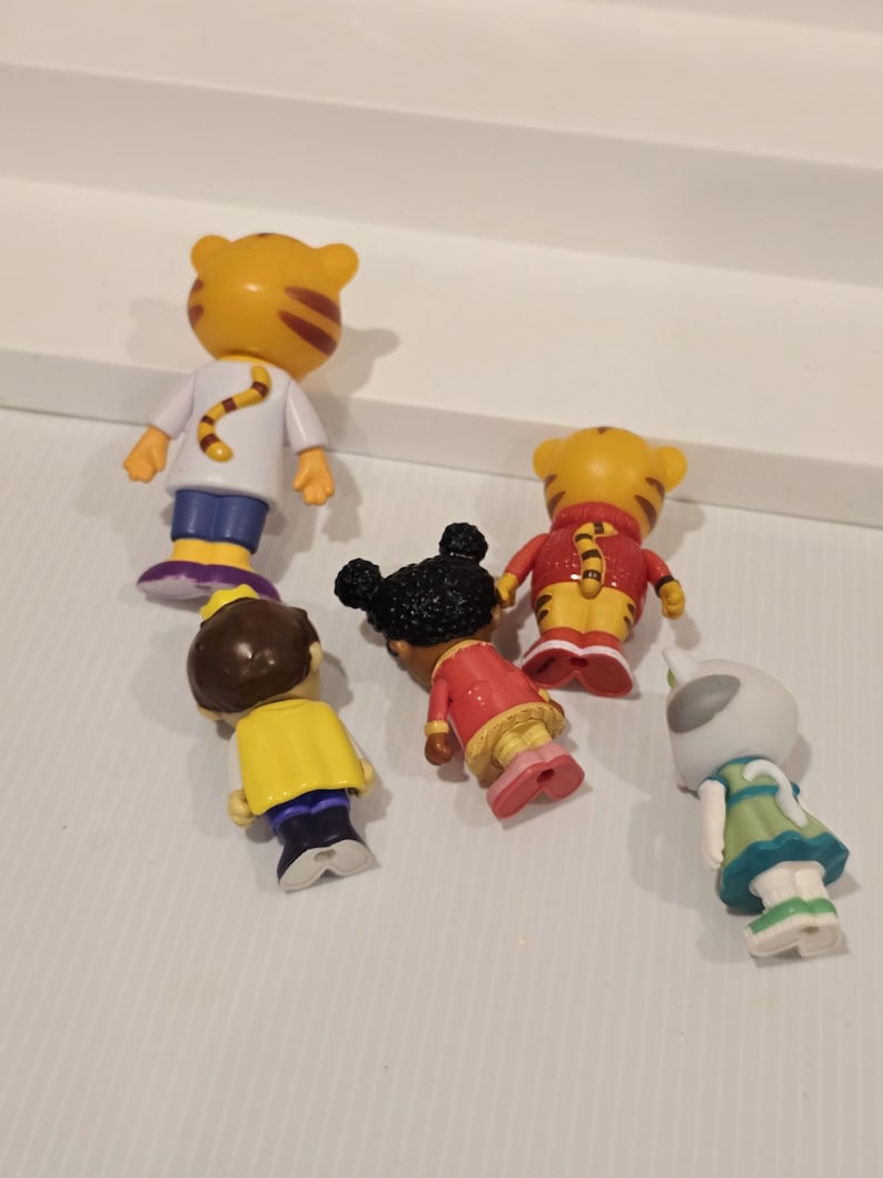 May include: A collection of small, colorful figurines featuring characters from a children's animated series. The figures include a tiger, a girl with black hair, and other characters in various outfits. The figurines are made of plastic and are brightly colored.