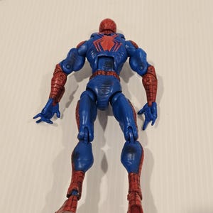 Pode incluir: Figura de a&ccedil;&atilde;o azul e vermelha de um super-her&oacute;i, vista por tr&aacute;s. A figura tem um emblema de aranha vermelho nas costas e detalhes vermelhos nos bra&ccedil;os e pernas. A figura est&aacute; em pose com os bra&ccedil;os ao lado.