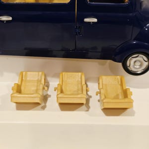 May include: A dark blue toy car with three tan-colored seats in front of it. The car has a steering wheel and a detailed interior. The seats are approximately 3 inches wide.