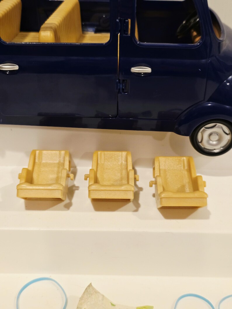 May include: A dark blue toy car with three tan-colored seats in front of it. The car has a steering wheel and a detailed interior. The seats are approximately 3 inches wide.