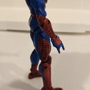 Pode incluir: Figura de a&ccedil;&atilde;o azul e vermelha de um super-her&oacute;i. A figura tem uma constru&ccedil;&atilde;o muscular, com se&ccedil;&otilde;es vermelhas nos bra&ccedil;os, pernas e p&eacute;s, e azul no torso e nas articula&ccedil;&otilde;es. A figura est&aacute; em uma pose din&acirc;mica.