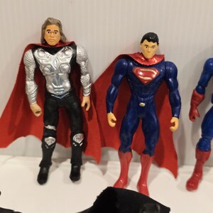 May include: A collection of superhero action figures, including Thor and Superman. Thor has long blonde hair, a silver chest plate, and a red cape. Superman wears a blue suit with a red cape and boots. Other figures are partially visible.