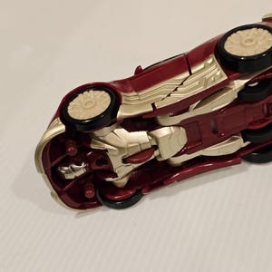 May include: A red and gold toy car with black wheels. The car has a sleek design with gold accents and a detailed undercarriage. The toy car is a collectible item.