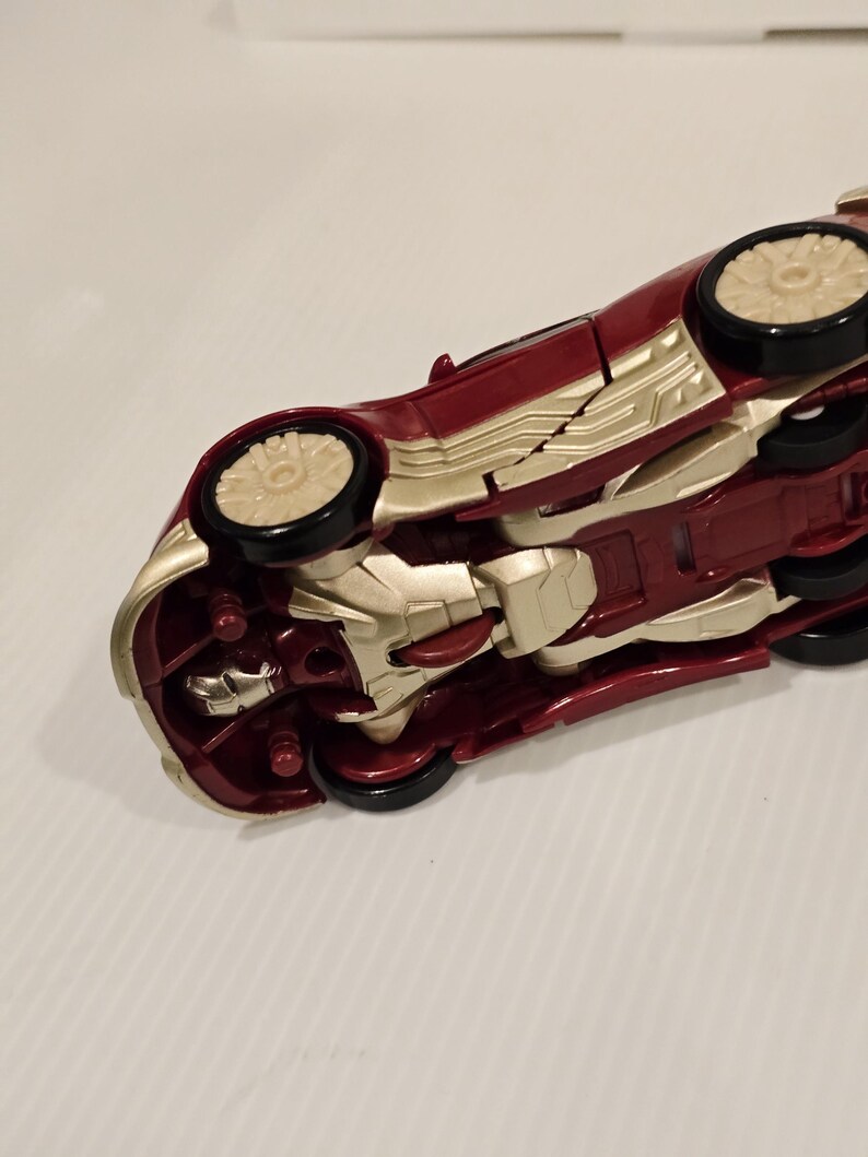May include: A red and gold toy car with black wheels. The car has a sleek design with gold accents and a detailed undercarriage. The toy car is a collectible item.