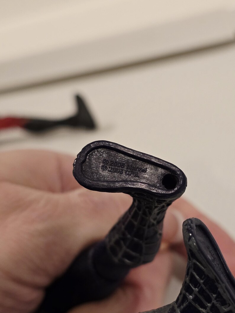May include: Close-up of a black action figure's foot, with the text "&copy; 2005 Marvel" and "&copy; 2005 CPII" imprinted on the sole. The figure has a textured, web-like design.