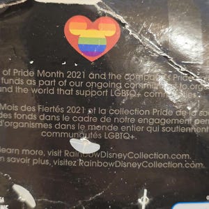 May include: A black product package featuring a rainbow-colored Mickey Mouse head inside a red heart. The text mentions Pride Month 2021 and support for LGBTQ+ communities. Visit RainbowDisneyCollection.com.
