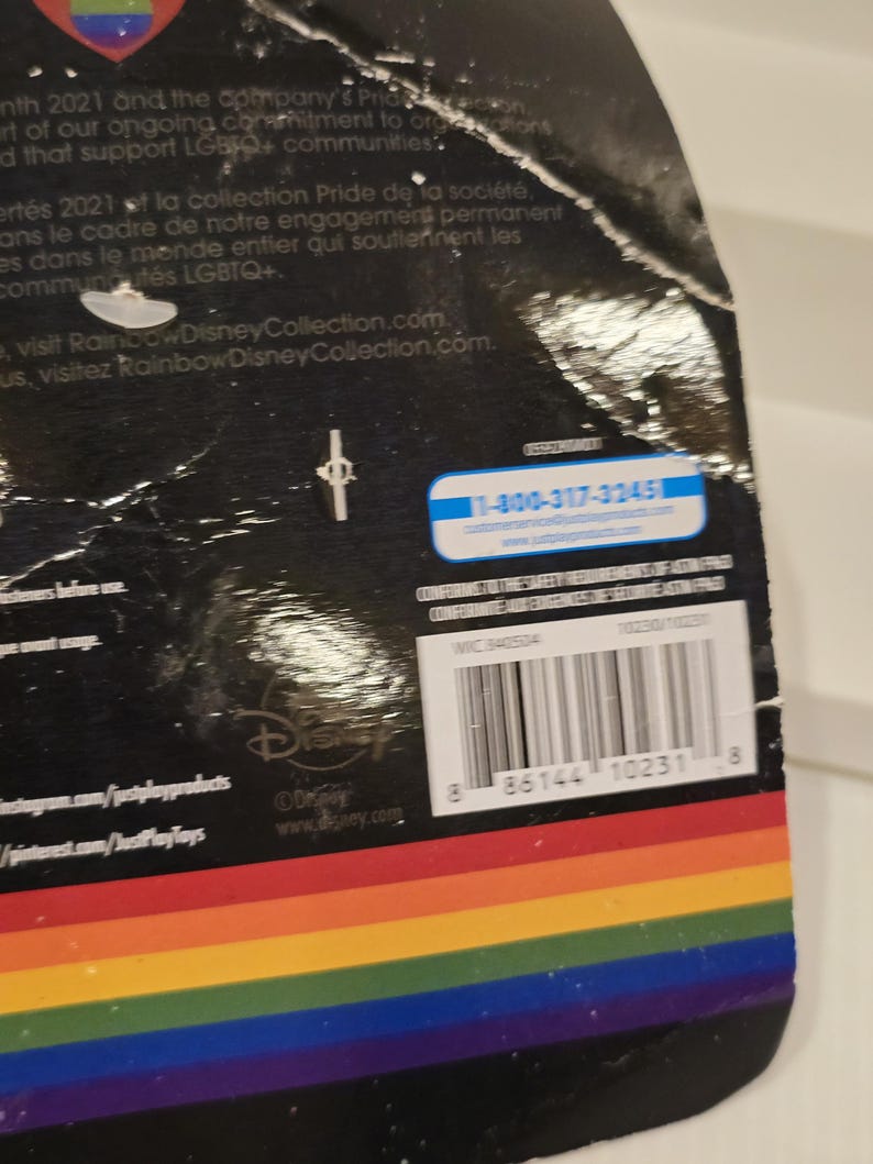 May include: A product package with a rainbow-colored stripe design at the bottom. The package has text in English and French, along with a barcode and the Disney logo. A customer service phone number is also visible.