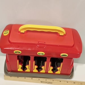 K&ouml;nnte beinhalten: Roter und gelber Spielzeugbus mit gelbem Griff oben. Das Spielzeug hat drei &Ouml;ffnungen vorne und drei runde Kn&ouml;pfe mit gr&uuml;n-gelben Designs. Ein Lineal ist vor dem Spielzeug platziert.