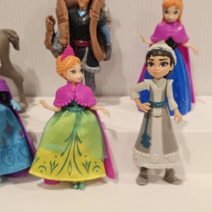 May include: A collection of miniature figurines featuring characters from the animated film "Frozen." The figures include Anna, Elsa, Kristoff, and other characters. The figurines are brightly colored and detailed, with each character wearing their signature outfits.
