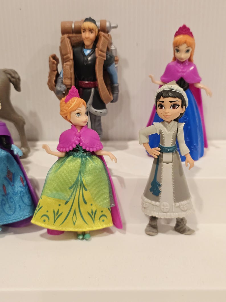 May include: A collection of miniature figurines featuring characters from the animated film "Frozen." The figures include Anna, Elsa, Kristoff, and other characters. The figurines are brightly colored and detailed, with each character wearing their signature outfits.