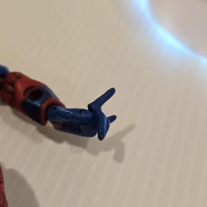 Pode incluir: Close-up do bra&ccedil;o azul e vermelho de uma figura de a&ccedil;&atilde;o. A m&atilde;o azul est&aacute; posada com os dedos indicador e m&eacute;dio estendidos, e o polegar e outros dedos curvados. O bra&ccedil;o da figura &eacute; vermelho e azul.