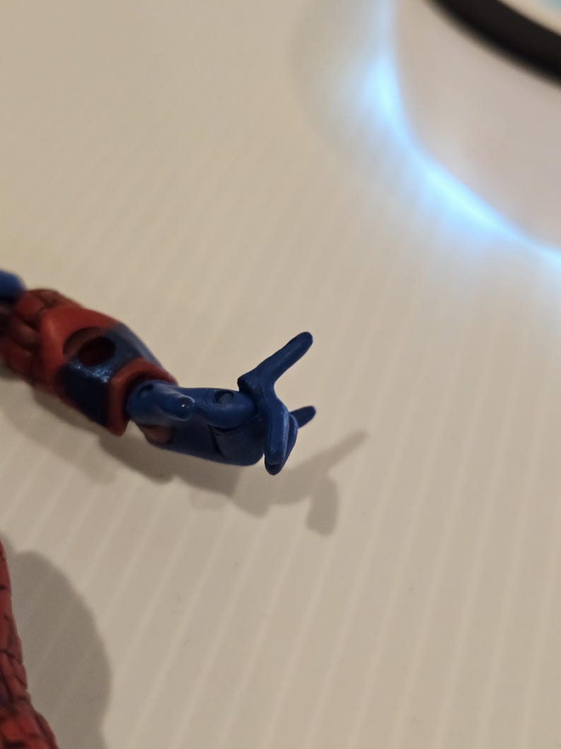 Pode incluir: Close-up do bra&ccedil;o azul e vermelho de uma figura de a&ccedil;&atilde;o. A m&atilde;o azul est&aacute; posada com os dedos indicador e m&eacute;dio estendidos, e o polegar e outros dedos curvados. O bra&ccedil;o da figura &eacute; vermelho e azul.