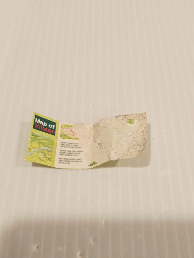 May include: A small, folded map labeled "Map of Village" with a green, yellow, and white landscape illustration. The map is creased and worn, with visible text and a detailed drawing of a village.