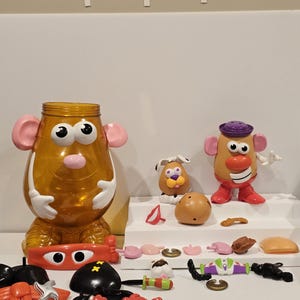 May include: A collection of Mr. Potato Head toy parts and accessories, including a large container shaped like the character's body. Various facial features, hats, and limbs are scattered around, with a complete Mr. Potato Head assembled.
