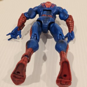 Pode incluir: Figura de a&ccedil;&atilde;o azul e vermelha de um super-her&oacute;i, vista de tr&aacute;s. A figura tem um corpo azul com detalhes vermelhos nos bra&ccedil;os e pernas. A cabe&ccedil;a &eacute; vermelha com um desenho de teia de aranha preta. As m&atilde;os s&atilde;o azuis.