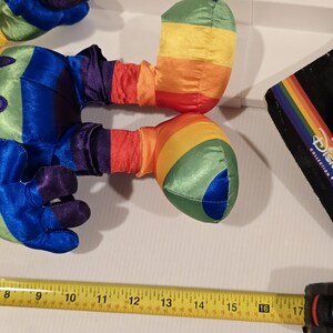 May include: A colorful plush toy with rainbow-striped arms and legs, and blue, purple, and green accents. The toy is next to a measuring tape showing 16 inches. A Disney Collection tag is visible.