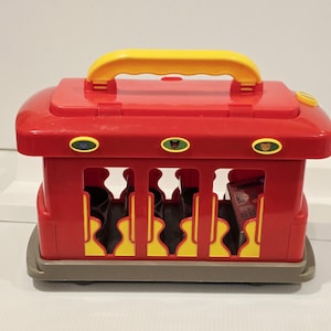 K&ouml;nnte beinhalten: Ein roter und gelber Spielzeugwagen mit gelbem Griff. Der Wagen hat Aussparungen mit gelben und schwarzen Akzenten. Der Wagen hat eine graue Basis und enth&auml;lt schwarze Objekte.