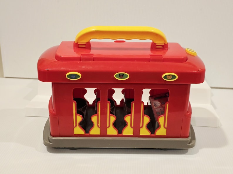 K&ouml;nnte beinhalten: Ein roter und gelber Spielzeugwagen mit gelbem Griff. Der Wagen hat Aussparungen mit gelben und schwarzen Akzenten. Der Wagen hat eine graue Basis und enth&auml;lt schwarze Objekte.
