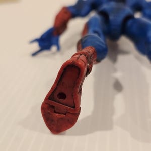 Pode incluir: Uma figura de a&ccedil;&atilde;o azul e vermelha de um super-her&oacute;i, deitada. A figura tem um fato azul com detalhes vermelhos nos bra&ccedil;os e nos p&eacute;s. O p&eacute; da figura est&aacute; em primeiro plano, mostrando a bota vermelha com um buraco.