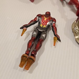 May include: A red, silver, and gold action figure of a superhero in a flying pose. The figure has a detailed design with a metallic finish. The figure has orange cone-shaped elements coming from the hands and feet.