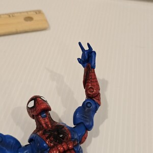 Pode incluir: Figura de a&ccedil;&atilde;o do Homem-Aranha em pose din&acirc;mica, com traje vermelho e azul e detalhes de teia de aranha. O bra&ccedil;o est&aacute; levantado, a m&atilde;o faz um gesto. Olhos brancos e emblema de aranha preta no peito.