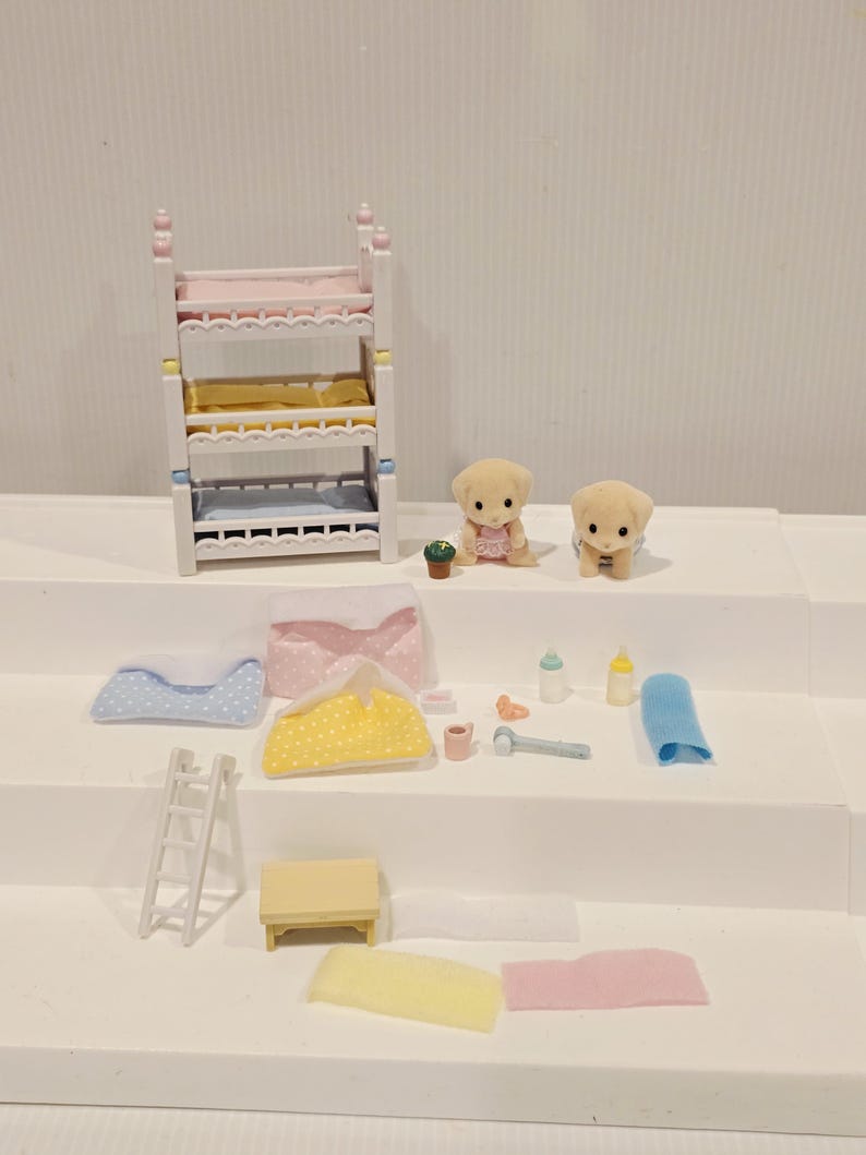 Puede incluir: Un juego de guarder&iacute;a en miniatura para casa de mu&ntilde;ecas con una litera, dos figuras de cachorros y varios accesorios. Incluye una mesita, una escalera, mantas, biberones y un pa&ntilde;o. La litera tiene detalles en rosa, amarillo y azul.
