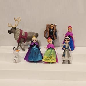 May include: A collection of miniature figurines featuring characters from the animated film "Frozen." The set includes Elsa, Anna, Kristoff, Olaf, and Sven. The figurines are dressed in their signature outfits, with vibrant colors and detailed designs.
