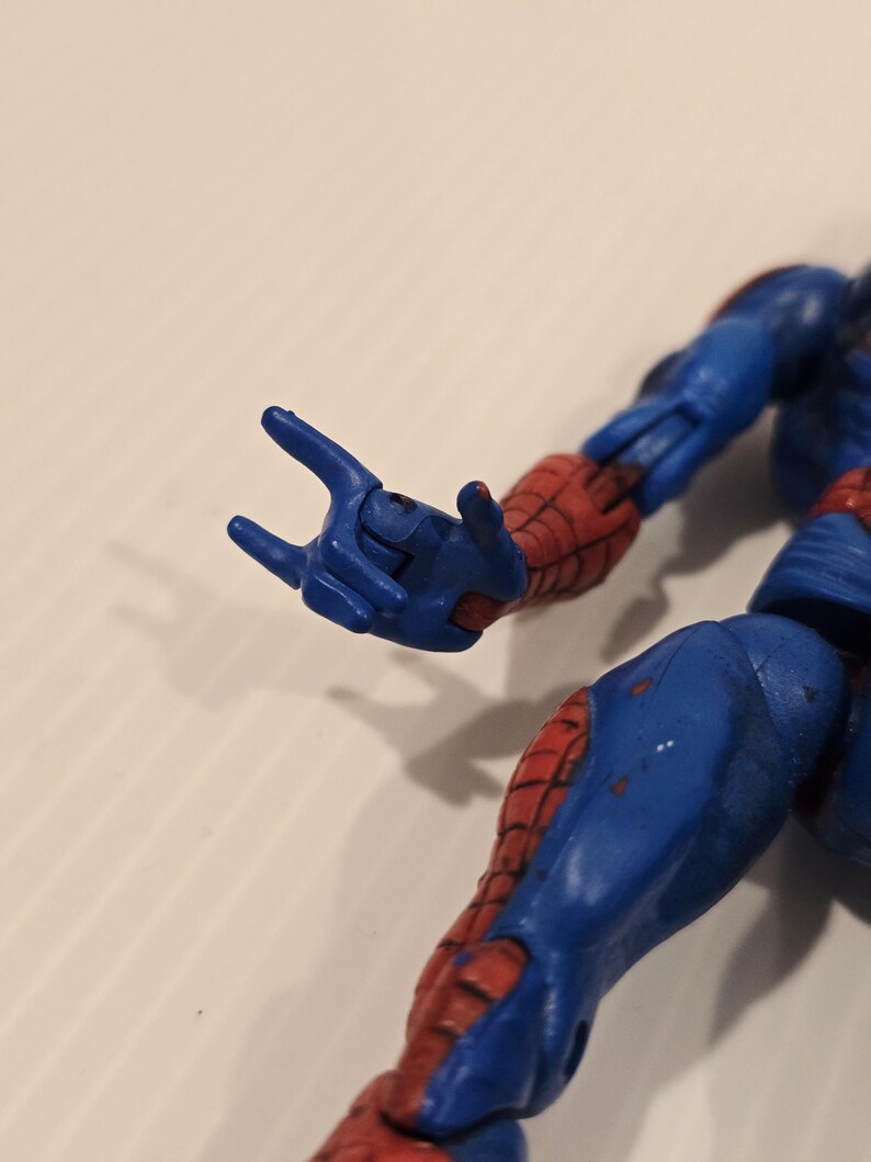 Pode incluir: Uma figura de a&ccedil;&atilde;o azul e vermelha de um super-her&oacute;i, com um gesto com a m&atilde;o. A figura tem um fato azul com detalhes vermelhos nos bra&ccedil;os e pernas. A figura est&aacute; numa pose din&acirc;mica, com uma m&atilde;o estendida.