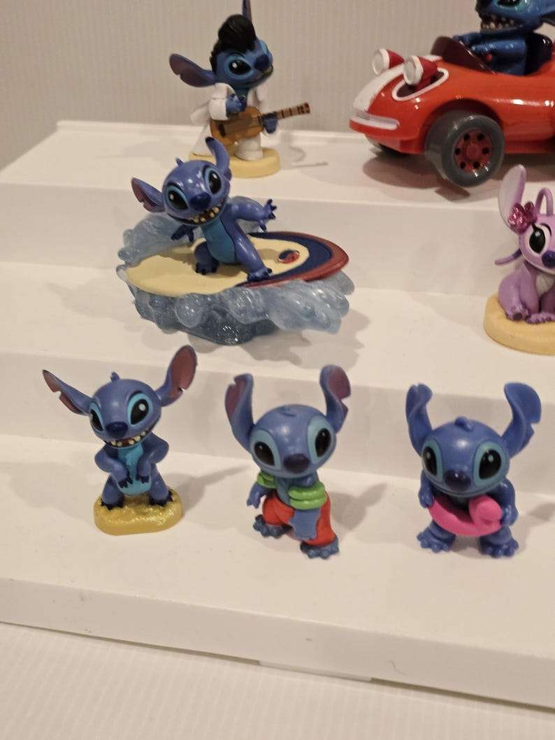 May include: A collection of blue Stitch figurines in various poses. One figurine surfs on a surfboard, while another plays a guitar. Other figurines are in different outfits, including a red race car.