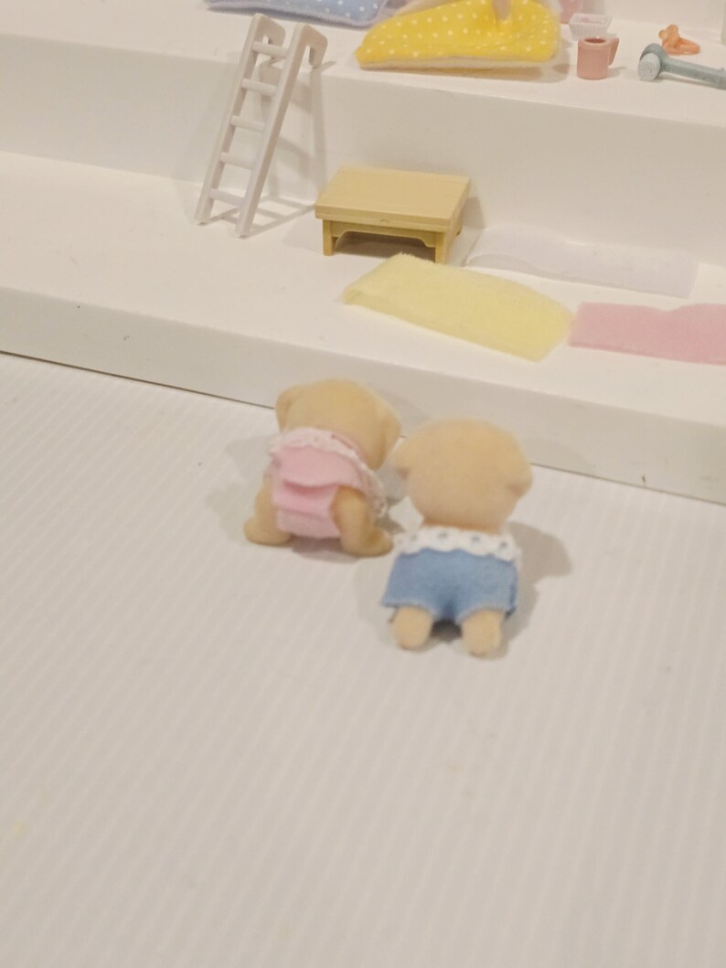 Puede incluir: Dos figuras de animales de juguete en miniatura, una con un atuendo rosa y la otra con pantalones cortos azules con ribete blanco. Las figuras son de color marr&oacute;n claro y parecen ser parte de un juego. Otros accesorios en miniatura son visibles.