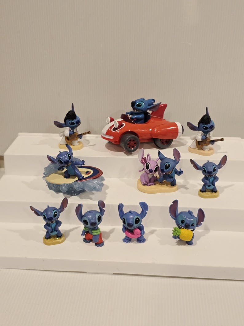 May include: A collection of blue Stitch figurines in various poses. Some figurines are playing a guitar, surfing, or driving a red car. Other figurines are holding a pineapple or wearing accessories.