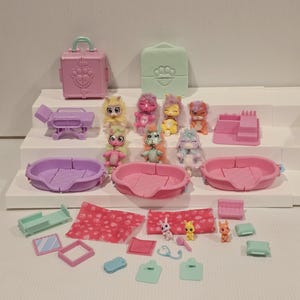May include: A collection of colorful toy pet accessories and figurines. Includes pink and purple pet beds, a pink suitcase, and small animal figures with various colors. Also includes a bed, mirror, and medical tools.
